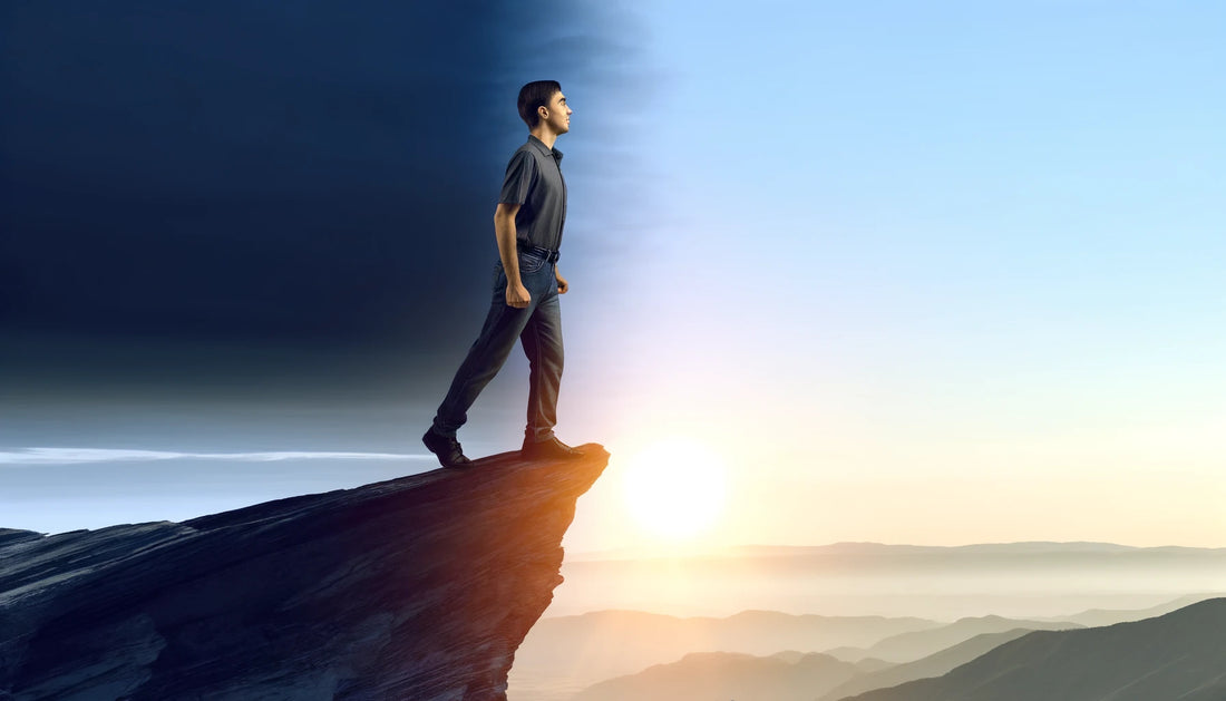 A person standing on a cliff edge at sunrise, looking determined and reflecting a sense of overcoming negative self-talk.